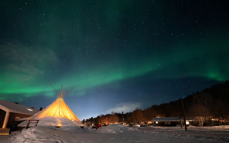 Lavvo tent glowing in the snow at night under the northern lights in northern Norway